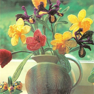 May include: A crocheted bouquet of flowers in a green and brown ceramic vase. The flowers are yellow, purple, red, and green. The vase has a textured surface.