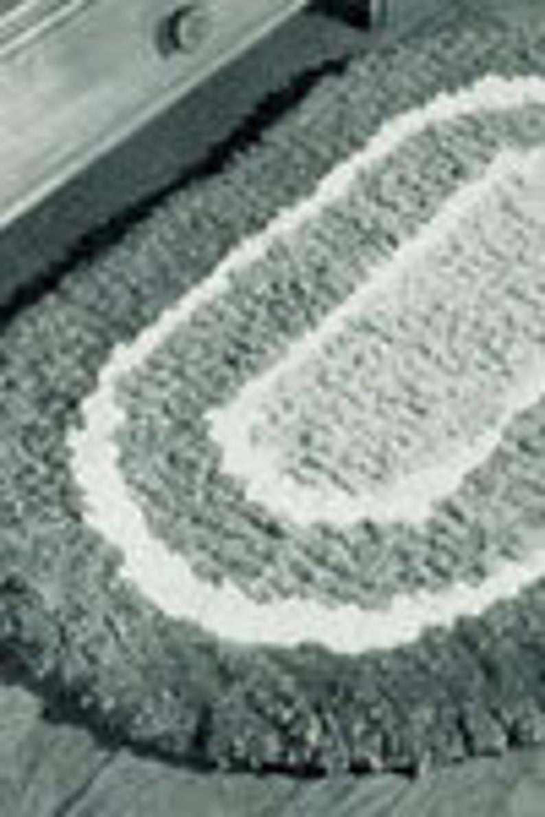 K&ouml;nnte beinhalten: Ein grauer und wei&szlig;er ovaler Teppich mit geflochtener Textur. Der Teppich hat einen wei&szlig;en Rand.