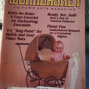 May include: The cover of a Workbasket magazine from August 1986 featuring a pink knitted baby blanket in a wicker baby carriage with a doll inside. The magazine cover features the text "Knits for Baby: A Cozy Coverlet, An Enchanting Ensemble, Try "Rag-Point" for Quick and Easy Place Mats, Ready, Set, Sail! Knit a Pair of Nautical Pullovers, Floral Fun Embroidered Bouquet on a Crocheted Afghan."