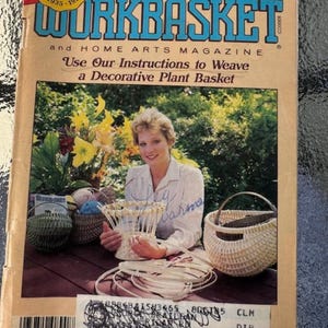 May include: A magazine cover featuring a woman holding a woven basket. The magazine is called "Workbasket" and is a home arts magazine. The cover text reads "Use Our Instructions to Weave a Decorative Plant Basket".