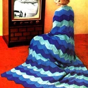 May include: A woman sits in front of a television wearing a blue, teal, and white chevron patterned knitted throw blanket.
