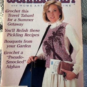 May include: The Workbasket magazine cover from June/July 1986 features a woman wearing a crocheted vest and a white blouse. The cover text includes "Crochet this Travel Tabard for a Summer Getaway", "You'll Relish these Pickling Recipes", "Bouquets from your Garden", and "Crochet a "Pseudo-Smocked" Afghan".