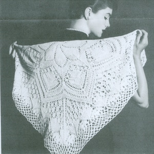 May include: A white, intricately crocheted shawl with a geometric and floral pattern. The shawl is held up, showcasing its delicate openwork design and textured details. The shawl's edges have a scalloped trim.