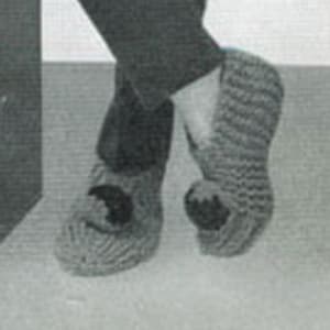 May include: A pair of grey knitted slippers with black felt appliques in the shape of a bat. The slippers have a pointed toe and a flat sole.
