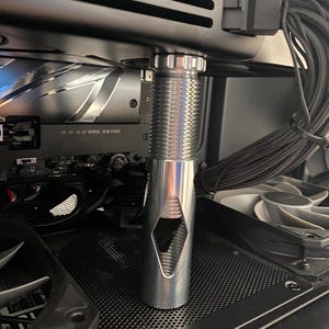 May include: A silver computer component with a threaded top and a diamond-shaped cutout. The component is installed inside a computer case, with other components visible in the background.