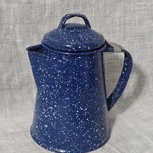 May include: A blue speckled enamelware coffee pot with a lid and handle. The pot has a classic design, perfect for camping or rustic kitchen decor. The blue color is accented with white speckles.