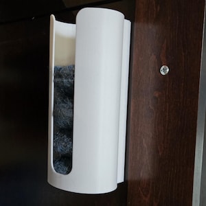 May include: White plastic dispenser mounted on a dark wood cabinet. The dispenser holds a stack of gray cleaning scrubbers.