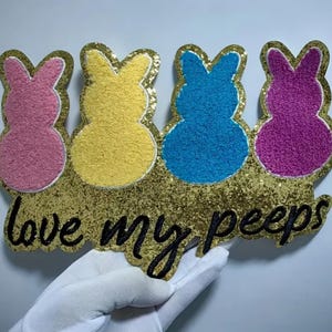 May include: A gold glitter background with four colorful felt bunny shapes and the text "love my peeps".