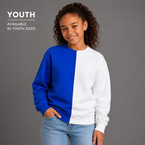 May include: A long-sleeve crewneck sweatshirt featuring a split-color design with a solid royal blue right side and a solid white left side. The text YOUTH AVAILABLE IN YOUTH SIZES is printed in white in the upper left corner of the image.