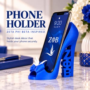 May include: A bright blue high-heeled shoe shaped phone holder featuring a white bow and dove accent at the toe. The heel is formed by the letters ZΦB. A smartphone is resting in the holder, displaying the ZΦB logo and a dove graphic on its screen.