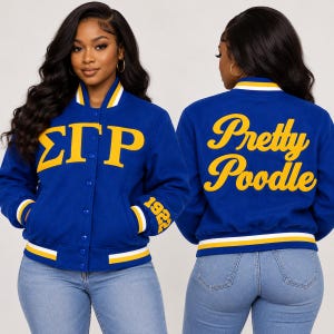 May include: A royal blue varsity jacket featuring yellow Greek letters ΣΓΡ on the front, the number 1922 on the sleeve, and the text Pretty Poodle in yellow script on the back. The jacket has a snap-button closure and white and yellow striped trim.