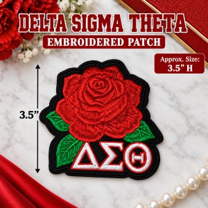 Peut inclure: Un écusson brodé représentant une rose rouge avec des feuilles vertes au-dessus des lettres grecques blanches Delta, Sigma et Theta. L'écusson a une bordure noire et mesure 8,89 cm de hauteur, comme indiqué par une flèche de mesure.