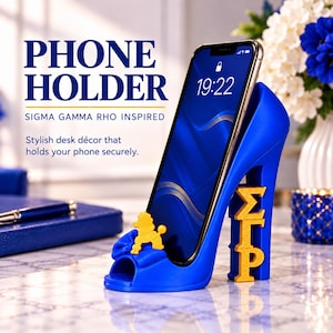 May include: A royal blue high-heeled shoe phone holder featuring a gold poodle emblem on the toe and gold Greek letters Sigma Gamma Rho on the heel. The text PHONE HOLDER SIGMA GAMMA RHO INSPIRED Stylish desk décor that holds your phone securely is visible.