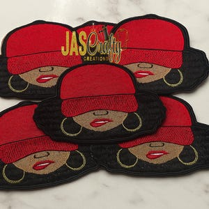 May include: Embroidered patches featuring a woman wearing a red cap, gold hoop earrings, and red lipstick. The patches have black hair and a tan face. The text "JAS Crafty Creations" is in gold lettering.