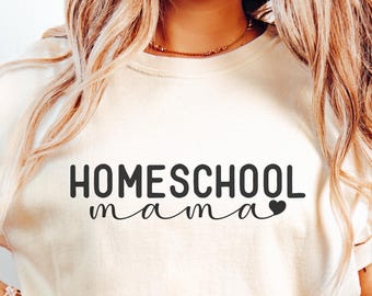 May include: A cream-colored short-sleeve t-shirt featuring the black text "HOMESCHOOL mama" with a small heart icon at the end of the word mama, paired with light blue denim jeans.