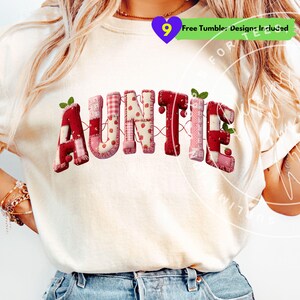 Puede incluir: Camiseta color crema con la palabra "AUNTIE" en un diseño de patchwork. Las letras son rojas, rosas y blancas, con estampados de fresas y cuadros. Cada letra tiene un efecto 3D y está adornada con hojas verdes.