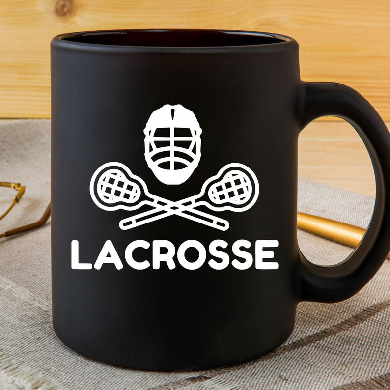 Op de afbeelding: Zwarte koffiemok met een wit lacrosse-stick- en helmdesign. De tekst "LACROSSE" is onder het ontwerp gedrukt.