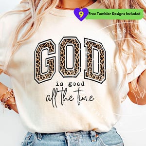 May include: Cream-colored sweatshirt with the words "GOD" in a bold, block letter design with a leopard print pattern. Below the word "GOD" is the phrase "is good all the time" in a handwritten font. A purple heart with the number 9 is in the top left corner.