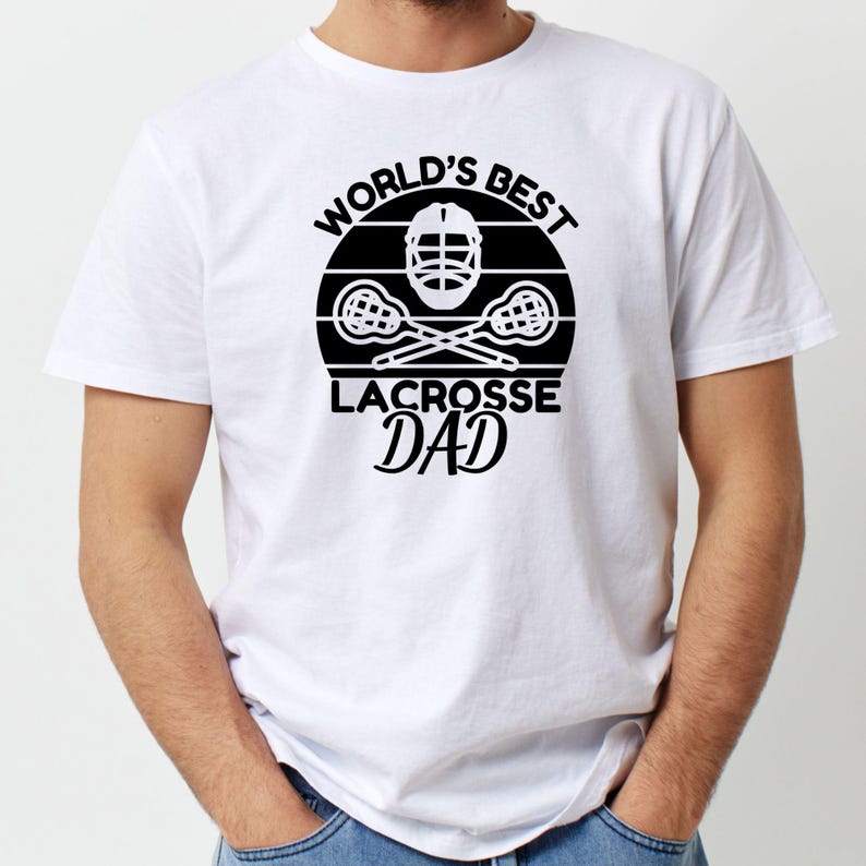 Op de afbeelding: Wit T-shirt met een zwart grafisch ontwerp met de tekst "World's Best Lacrosse Dad" met een lacrosse-stick en helm.