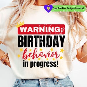 May include: A cream-coloured t-shirt featuring the text "WARNING: BIRTHDAY behavior in progress!" in black and red, with yellow star accents. A small gold crown graphic is above the word "WARNING".