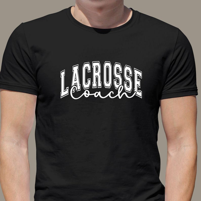 Op de afbeelding: Zwart T-shirt met witte tekst die "Lacrosse Coach" zegt in een lettertype in varsity-stijl.