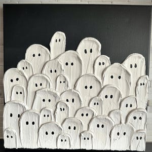May include: A textured white painting on a black canvas features a crowd of stylized ghosts. Each ghost has a simple, oval shape with two black dot eyes. The artwork is a unique, handmade piece, perfect for Halloween or spooky decor.