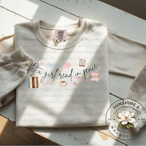 May include: Cream-colored sweatshirt with the text "Let a girl read in peace" and various book-themed graphics. The sweatshirt has a crew neck and long sleeves. A circular logo with a flower is on the sleeve.