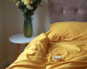 May include: A yellow bedspread with a small white jar on top. The bedspread is made of soft, smooth fabric. The bed is made up with a yellow pillow and a brown headboard.