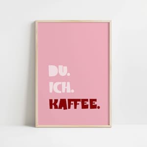 Framed poster with bold German text “Du. Ich. Kaffee.” in playful retro fonts on a solid pink background, leaning against a white wall.