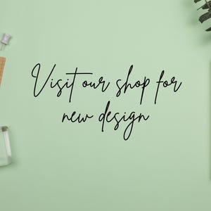 May include: A light green background with the handwritten text "Visit our shop for new design" in black cursive script. A push pin, a small notepad, and a clear block are in the image.