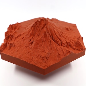 Puede incluir: Modelo topográfico tridimensional de color terracota de una cordillera. El modelo, de forma cuadrada, presenta crestas, valles y picos detallados, mostrando el paisaje natural. El modelo se encuentra sobre un fondo blanco.