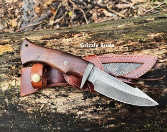 May include: A brown wooden handled knife with a leather sheath. The knife has a Damascus steel blade and the sheath has a snakeskin pattern. The text "Grizzly Knife" is visible in the image.