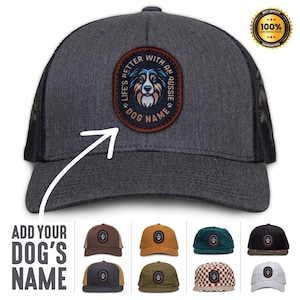 May include: A black and gray trucker hat with a brown patch featuring a dog's head and the text "Life's Better With An Aussie Dog Name". The hat is shown with a variety of different colored patches.