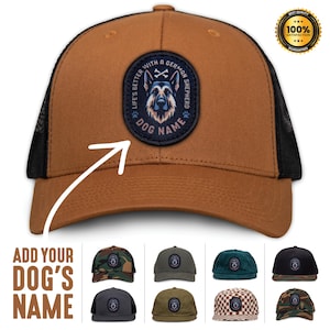 Może przedstawiać: Brązowa czapka typu trucker z czarną siatką z tyłu i naszywką z psem owczarkiem niemieckim. Na naszywce widnieje napis "Life's Better With A German Shepherd" i "Dog Name". Czapka ma zakrzywiony daszek i zapięcie na zatrzask.