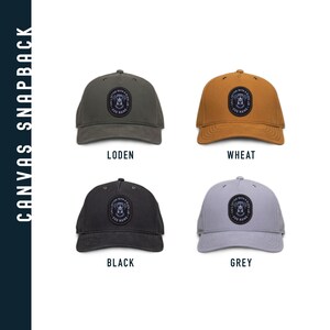 May include: Four canvas snapbacks in different colors: black, grey, wheat, and loden. Each hat features a black and white embroidered patch with a dog's head and the text "I'D RATHER BE WITH A DOG NAMED..."
