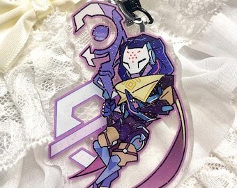 May include: A clear acrylic keychain featuring a purple and blue character design with a white mask and a staff. The keychain has a black clasp and a glittery finish. The character is holding a staff.