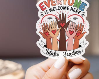Può includere: Un adesivo bianco con il testo "Everyone is welcome here" in lettere arcobaleno. L'adesivo presenta anche cinque mani di diversi toni della pelle che si alzano con cuori nei loro palmi. Il testo "Idaho Teacher" è nella parte inferiore dell'adesivo.