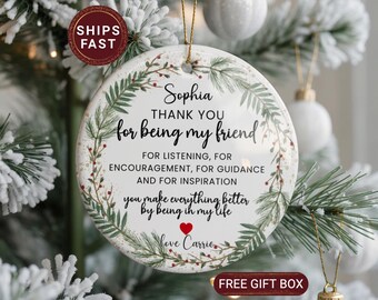 May include: A white ceramic Christmas ornament with a gold string, featuring a heartfelt message. The ornament is decorated with a green and red floral wreath. Text includes "Sophia, Thank you for being my friend" and a personal message.
