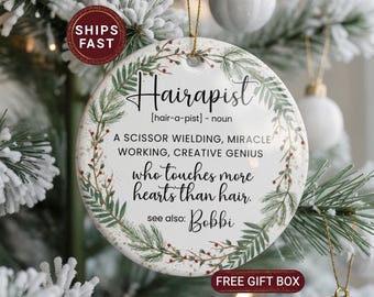 May include: A round ceramic ornament with the word "Hairapist" in black script, surrounded by a green and red floral design. The text defines "Hairapist" and includes the phrase "who touches more hearts than hair."