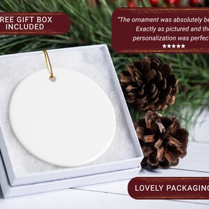 May include: A white ceramic ornament with a gold string, presented in a white gift box. The ornament is round and blank, ready for personalization. The packaging is described as "Lovely".