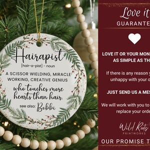 May include: A round, white ceramic ornament with the word "Hairapist" in black script. The ornament has a botanical wreath design and text that reads "A scissor wielding, miracle working, creative genius who touches more hearts than hair."