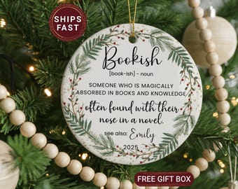 May include: A round, white ceramic ornament with the word "Bookish" in black script. The ornament has a botanical design with green leaves and red berries. Text on the ornament defines "Bookish" and includes the name "Emily" and the year "2025".