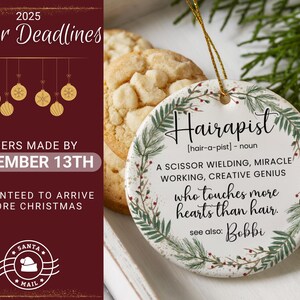 May include: A round, white ceramic ornament with the word "Hairapist" in black script, surrounded by a green and red leaf design. The ornament has text that reads "A scissor wielding, miracle working, creative genius who touches more hearts than hair."