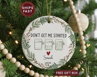 May include: A round, white ceramic Christmas ornament with the text "DON'T GET ME STARTED" and three jar illustrations. The ornament includes the name "Sarah" and the year "2025". It is decorated with a green and red floral border and a gold hanging string.