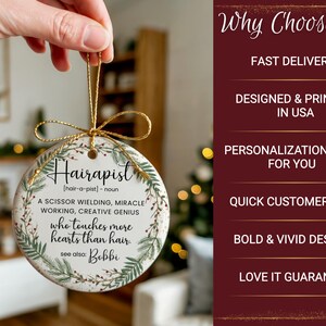 May include: A round, white ceramic ornament with the word "Hairapist" in black script. The ornament has a gold string for hanging and is decorated with green and brown botanical elements. Text on the ornament describes a hair stylist.