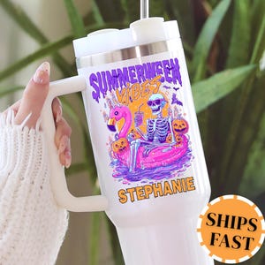 May include: White travel mug with a handle featuring a colorful graphic. The design includes a skeleton floating on a pink flamingo floatie, the words "Summerween Vibes," and the name "Stephanie."