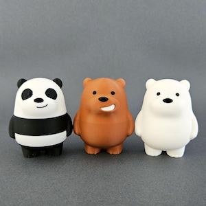 Peut inclure: Trois figurines de personnages d'ours de dessin animé : un panda avec des marques noires et blanches, un ours brun et un ours polaire blanc. Chaque ours a une expression faciale distincte et se tient debout. Le fond est gris uni.