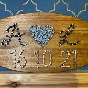 May include: A wooden sign with the letters A & L in black string art, a heart in blue string art, and the date 16.10.21 in silver string art.