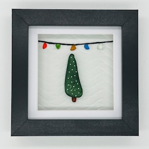 May include: A framed artwork featuring a green Christmas tree made of sea glass with white polka dots. The tree is decorated with a string of colorful lights.