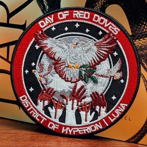 May include: Circular patch with the text "DAY OF RED DOVES" and "DISTRICT OF HYPERION I LUNA". The patch features a white dove with red wings and a green olive branch, surrounded by other doves and red hands.
